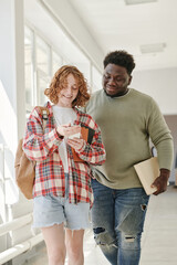 Wall Mural - Two teenage classmates in casualwear discussing curious stuff in smartphone held by cute smiling girl after lessons