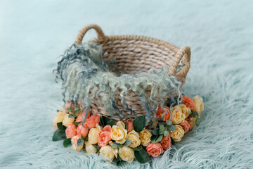 Shoot set up with basket decor for newborn studio photoshoot filled with fur and a lot of flowers and blue wool blanket on the turquoise background. Photo zone for a photo session of newborns. 