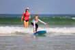Little surf girl - young surfer learn to ride on surfboard with instructor at surfing school. Active family lifestyle, kids water sport lessons, swimming activity in summer camp. Vacation with child