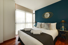 Bedroom With A Double Bed Decorated With Blue Wall, Design Mirror, Cushions And White Towels