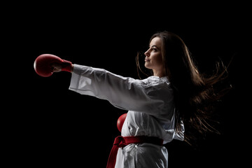 Wall Mural - girl exercising karate punch wearing kimono and red gloves against black background..