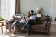Cheerful 30s couple relaxing on sofa at home spend time on internet using smartphone, watch video laughing enjoy carefree pastime with modern wireless technology. Mobile application usage, fun concept