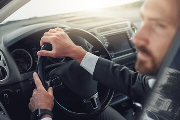 Handsome businessman in grey suit is riding behind steering wheel of car