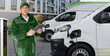 © scharfsinn86 - A man with a digital tablet stands next to electric delivery vans at electric vehicle charging stations