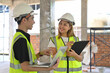 © saltdium - Portrait of Two Construction Engineers or Architects wearing white safety helmet and reflective clothing discussing at work with laptop on construction site.