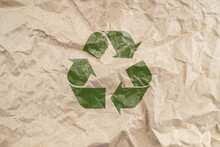 Recycled Brown Creased Paper Background From A Paper Packing With Green Recycling Symbol. Ecology Environmental Safety Concept
