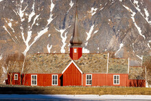 Norway, Lofoten Wooden Red Church With Snowy Mountains On The Background. Sunny Weather With Blue Sky