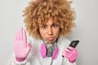 Leinwandbild Motiv Serious female scientist keeps palm raised wears hazmat protective suit holds mobile phone tries to prevent you from biological hazard focused attentively isolated over grey background. Pandemic
