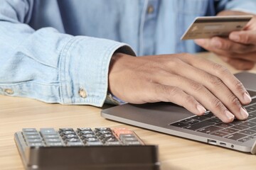 Businessman holding a credit card to pay taxes on a laptop. and a calculator on the desk. tax management concepts