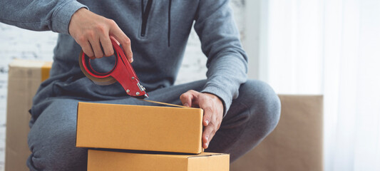 Detail of packing cardboard boxes while moving house. Young man packing box, indoors young male warehouse worker packing boxes for shipment. 