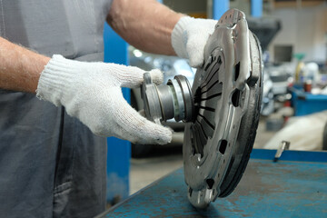 An auto mechanic holds a clutch kit. Compliance and integrity control of the drive disc, the driven disc and the exhaust bearing. Repair and maintenance in a car service center.