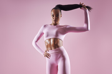 Wall Mural - Attractive African woman in sports clothing adjusting her hair against pink background