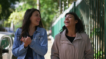 Two happy female friends walking outside. Carefree girls walk in urban street together