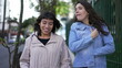 © Marco - Two women in conversation walking in city street. Female friends talking