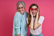 Leinwandbild Motiv Happy mother and adult daughter in funky eyeglasses having fun against pink background