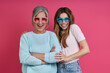 Leinwandbild Motiv Playful mother and adult daughter in funky eyeglasses standing against pink background