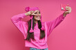 Leinwandbild Motiv Beautiful young woman in funky hat making selfie and gesturing against pink background