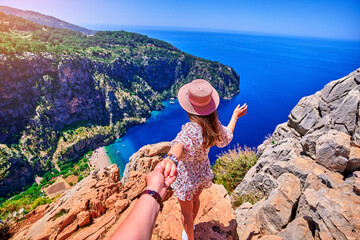 Wall Mural - Girl traveler stands on hill rock over blue sea bay in Turkey, butterfly valley. Enjoy holiday vacation and follow me to beautiful traveling places