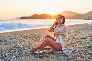 Calm serene alone woman with closed eyes enjoys of listening relax traveling music on the seashore at sunset time. Happy beautiful moment life