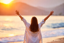 Back Of Calm Serene Happy Free Woman With Open Arms Enjoys A Beautiful Moment Life On The Seashore At Sunset Time