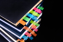 Close-up Of A Stack Of Office Notepads With Colorful Sticky Page Markers Sandwiched Between Pages On Dark Background