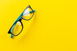 Stylish eyeglasses over yellow background. Glasses selection, eye test, vision examination at optician, fashion accessories concept. Top view, flat lay.
