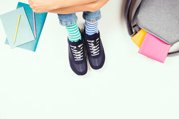 Kid wearing different pair of socks. Child in mismatched socks and colorful sneakers sitting on white background, with backpack, books and school supplies. Top view