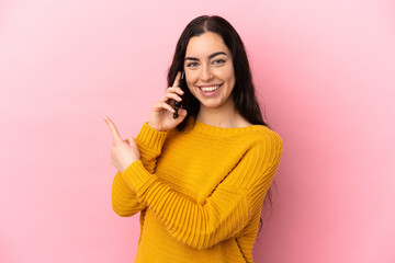 Young caucasian woman using mobile phone isolated on pink background pointing to the side to present a product