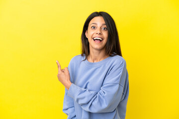 Wall Mural - Young caucasian woman isolated on yellow background surprised and pointing side