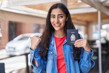 Young teenager girl holding canada passport pointing thumb up to the side smiling happy with open mouth