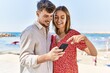 © Krakenimages.com - Young hispanic couple on vacation smiling happy using smartphone at the beach