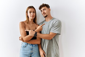 Wall Mural - Young beautiful couple standing together over isolated background pointing to both sides with fingers, different direction disagree