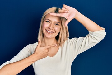 Poster - Beautiful blonde woman wearing casual sweater smiling making frame with hands and fingers with happy face. creativity and photography concept.