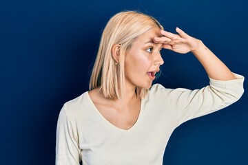 Poster - Beautiful blonde woman wearing casual sweater very happy and smiling looking far away with hand over head. searching concept.