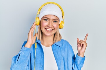 Beautiful blonde woman listening to music using headphones smiling happy pointing with hand and finger to the side