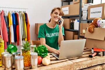 Young caucasian volunteer woman talking on the smartphone using laptop at charity center.