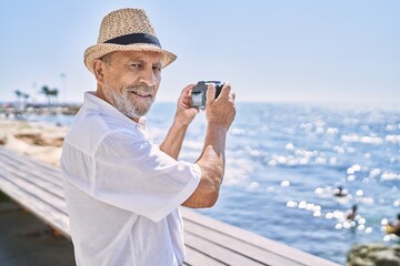 Canvas Print - Senior man smiling confident wearing summer hat using camera at seaside