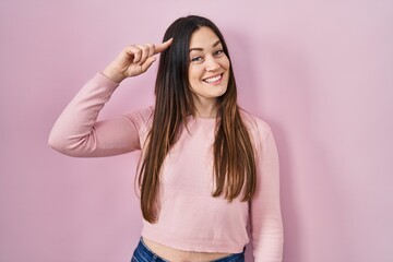 Sticker - Young brunette woman standing over pink background smiling pointing to head with one finger, great idea or thought, good memory