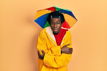 Poster - Young african american man wearing yellow raincoat shaking and freezing for winter cold with sad and shock expression on face