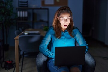 Wall Mural - Brunette woman working at the office at night afraid and shocked with surprise expression, fear and excited face.