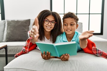 Poster - Two siblings lying on the sofa reading a book smiling friendly offering handshake as greeting and welcoming. successful business.