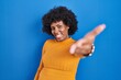 © Krakenimages.com - Black woman with curly hair standing over blue background smiling friendly offering handshake as greeting and welcoming. successful business.
