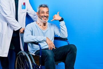 Poster - Handsome middle age man with grey hair on wheelchair wearing cervical collar smiling doing phone gesture with hand and fingers like talking on the telephone. communicating concepts.