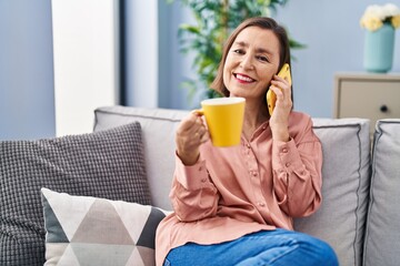 Sticker - Middle age woman drinking coffee and talking on the smartphone at home