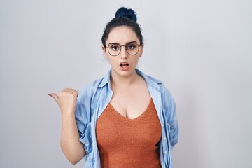 Canvas Print - Young modern girl with blue hair standing over white background surprised pointing with hand finger to the side, open mouth amazed expression.