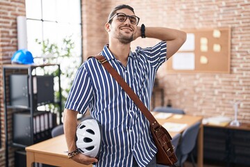 Canvas Print - Hispanic man with long hair working at the office holding bike helmet smiling confident touching hair with hand up gesture, posing attractive and fashionable