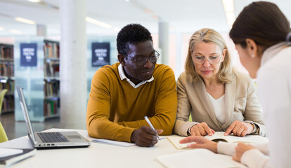 Students sitting in library, working with professor. High quality photo