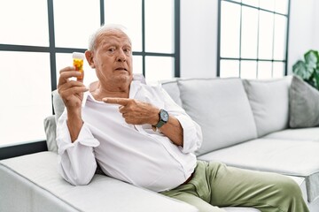 Poster - Senior man holding pills pointing aside worried and nervous with forefinger, concerned and surprised expression