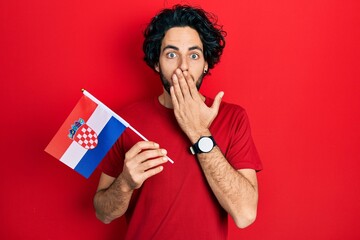 Poster - Handsome hispanic man holding croatia flag covering mouth with hand, shocked and afraid for mistake. surprised expression