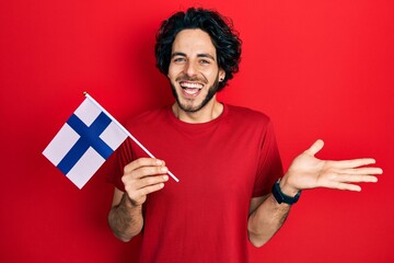 Sticker - Handsome hispanic man holding finland flag celebrating achievement with happy smile and winner expression with raised hand